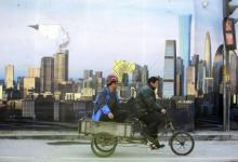 Des ouvriers chinois passent devant une affiche montrant le quartier des affaires de P&eacute;kin. Un ralentissement plus fort que pr&eacute;vu en Chine pourrait avoir des retomb&eacute;es encore plus vastes par le truchement des &eacute;changes et du tassement de la demande de mati&egrave;res premi&egrave;res (photo : Jason Lee/Reuters/Corbis) 