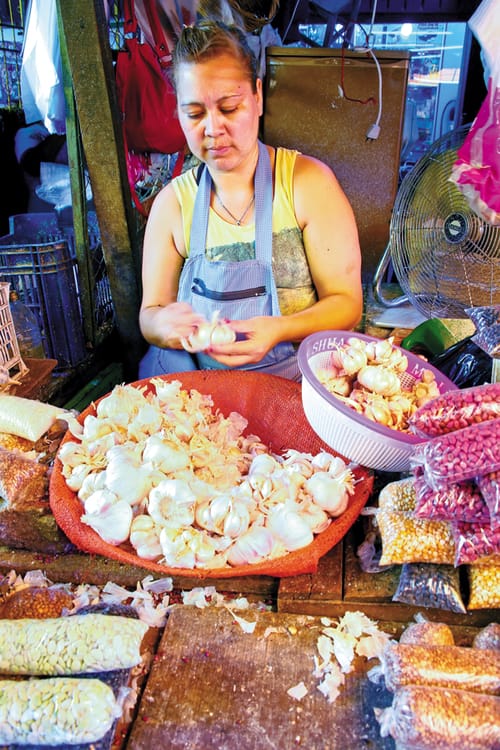 A woman peels garlic to sell in a small market stall
