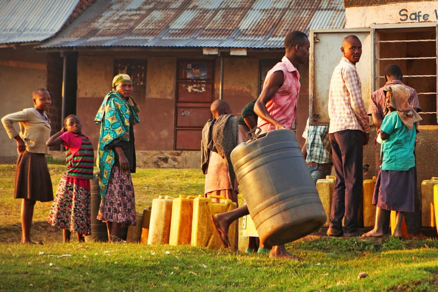 People carrying larger water barrels and waiting to fill jugs with safe water