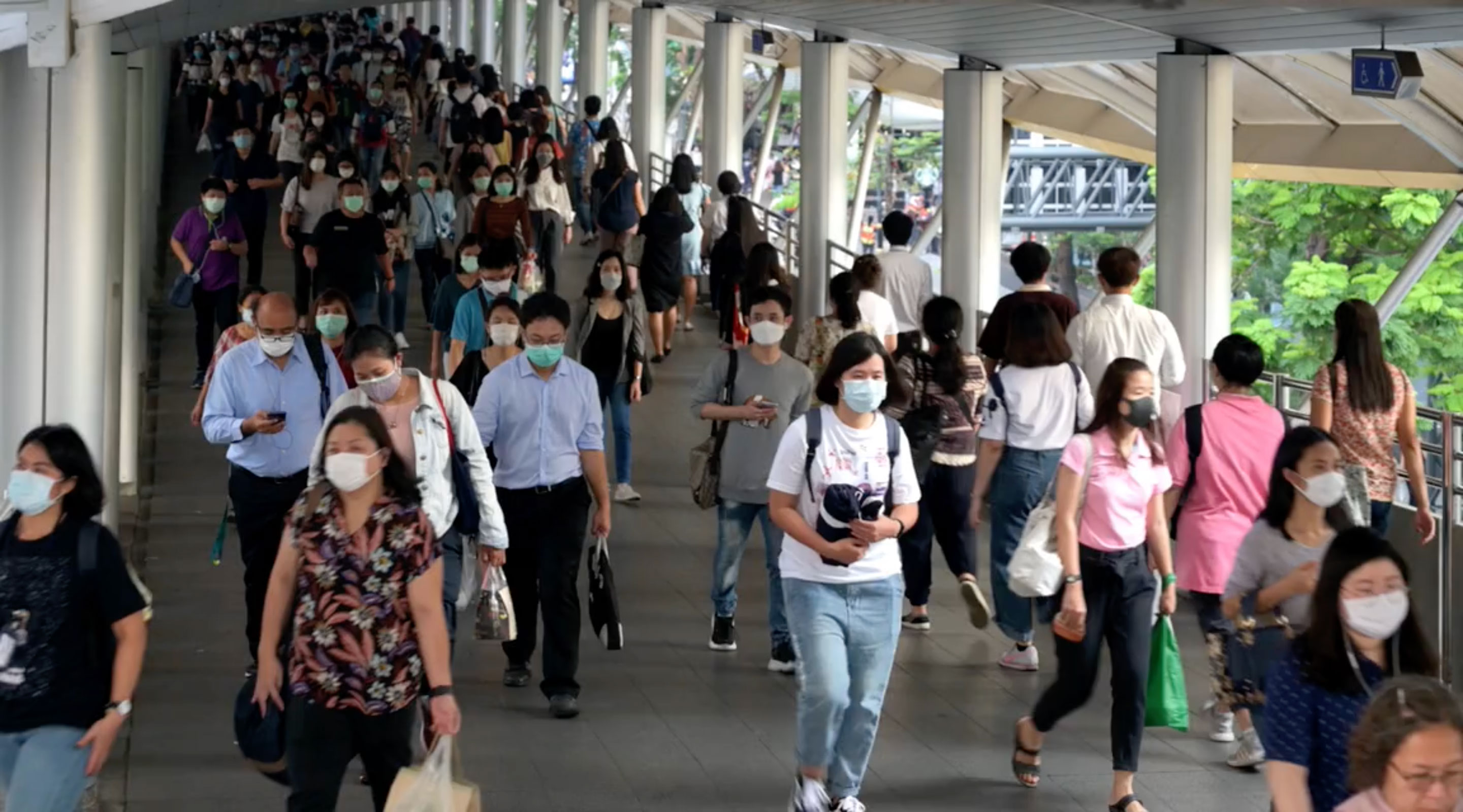 Many people walking across a busy pedestrian bridge and wearing masks