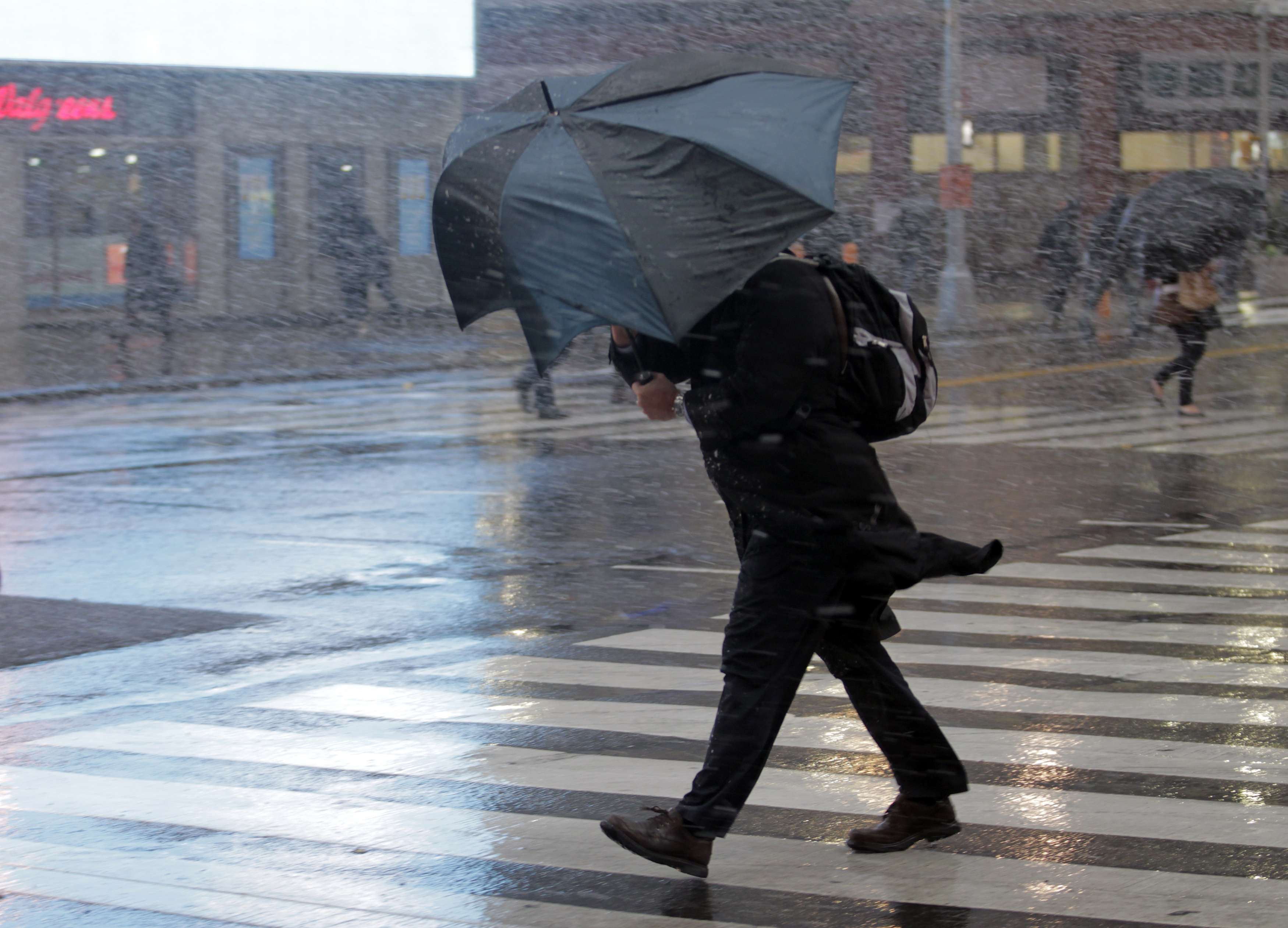 A man struggles with his umbrella in the wind and snow while crossing the street in New York