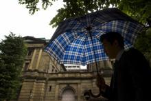 傘をさし日銀の前を歩く男性。IMFは、日銀は更なる緩和に備える必要があると述べた。（写真：Reuters/Thomas Peter/Corbis） 